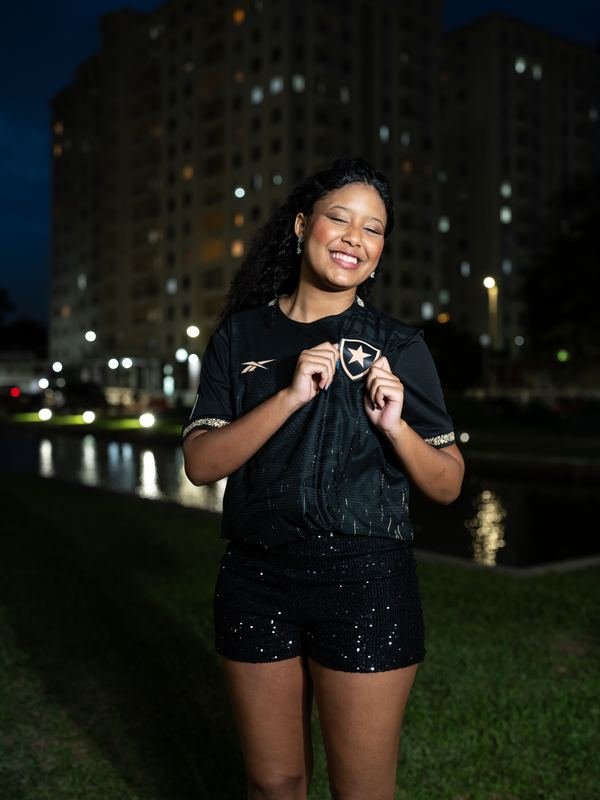 Larissa de camisa preta à noite, com prédios ao fundo